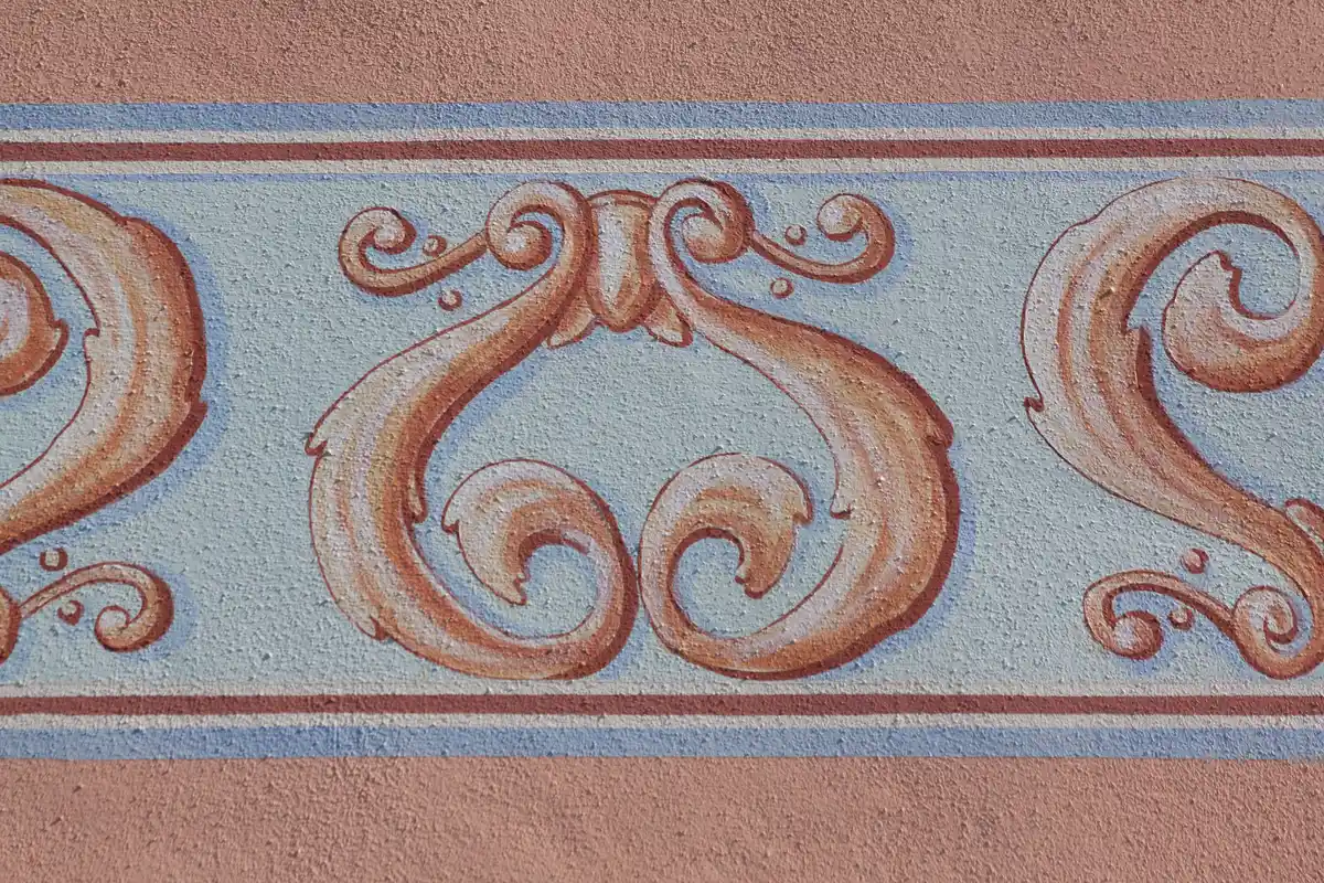 Malerische Sondertechniken: Detailaufnahme einer kunstvollen Schablonenarbeit, die klassische, ornamentale Muster auf einem strukturierten Untergrund zeigt.